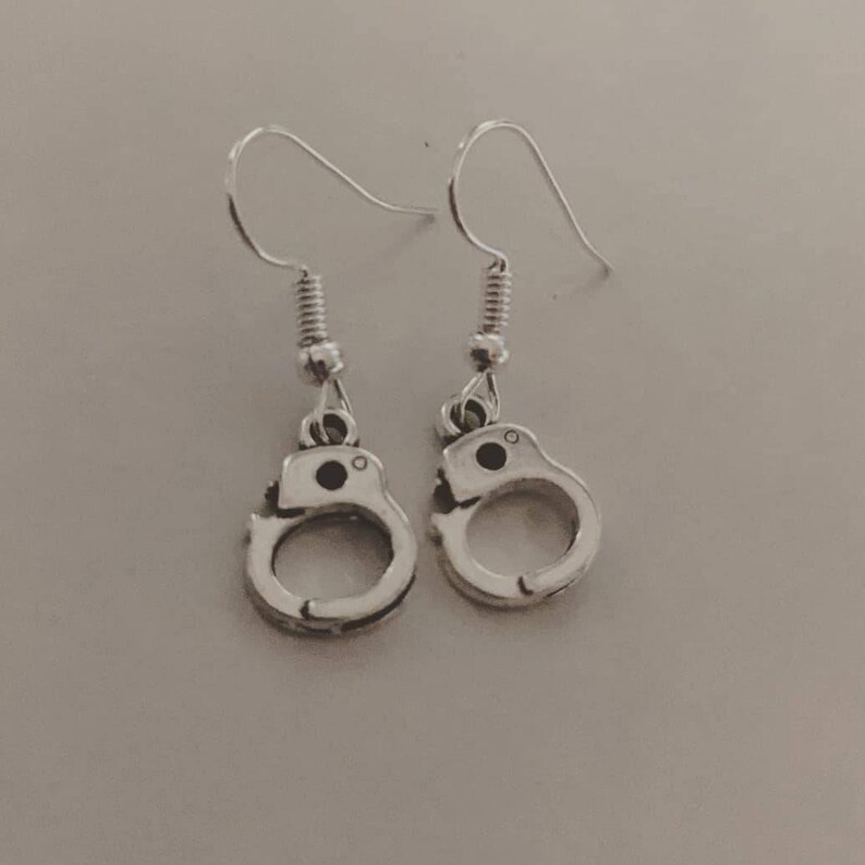 May include: A pair of silver dangle earrings featuring a handcuff design.