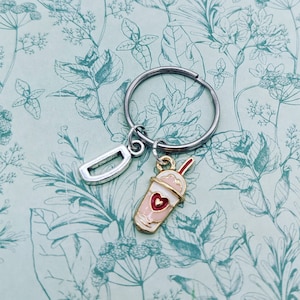 May include: A silver key chain with a letter D charm and a pink and white milkshake charm with a red heart and a red straw.