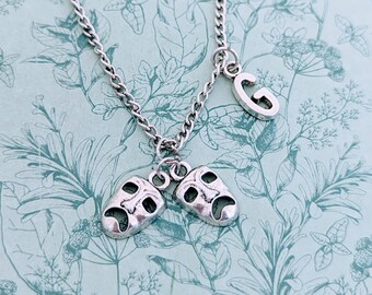 May include: A silver necklace with two silver charm pendants. One pendant is a happy face and the other is a sad face. The necklace also has a silver charm pendant with the letter G.