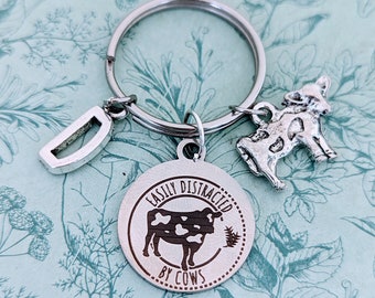 May include: Silver keychain with a cow charm and a round tag that says "Easily Distracted by Cows".