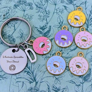 May include: A silver keychain with a round charm engraved with "Whatever Sprinkles Your Donut" and a donut graphic.  Also, several colorful donut charms in pink, yellow, purple, and blue with gold-colored trim.