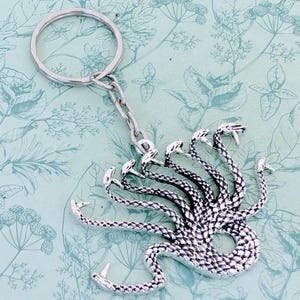 May include: Silver-toned keychain featuring a detailed depiction of a multi-headed serpent, a mythical creature often associated with Greek mythology.