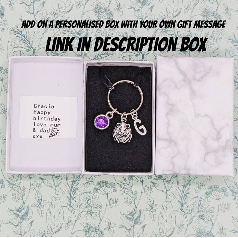 May include: A small gift box with a personalized message for Gracie. The box contains a keychain with a purple gem, a lion charm, and a letter G charm.