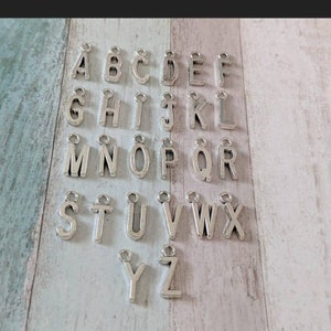 May include: Silver letter charms for jewellery making, featuring the alphabet from A to Z. Each charm has a small loop for attaching to a chain or bracelet.