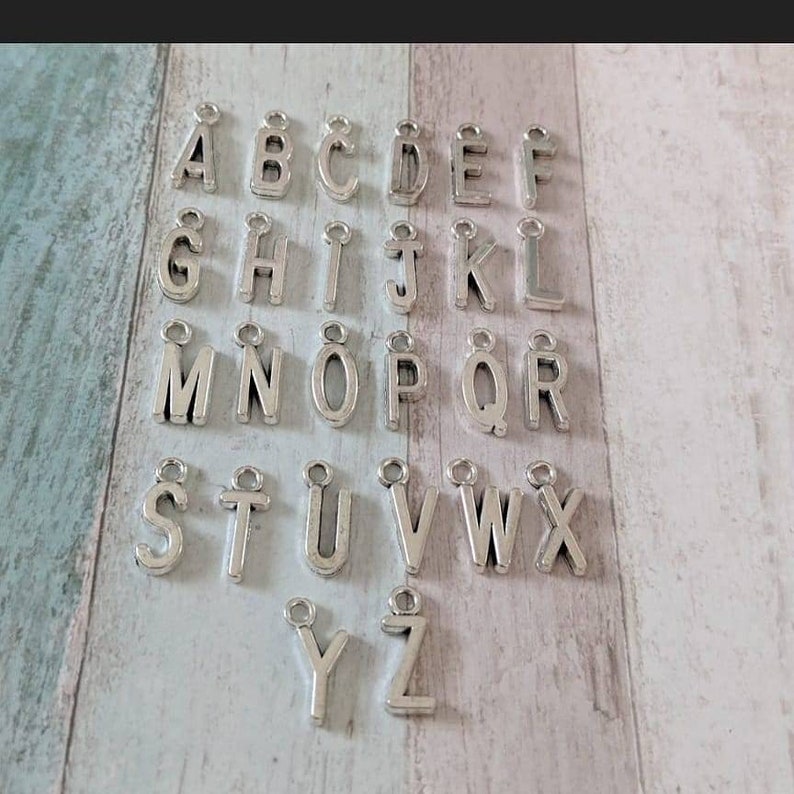 May include: Silver letter charms for jewellery making, featuring the alphabet from A to Z. Each charm has a small loop for attaching to a chain or bracelet.