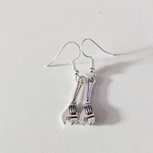 May include: A pair of silver wrench earrings. The earrings are in the shape of a wrench with a silver hook.