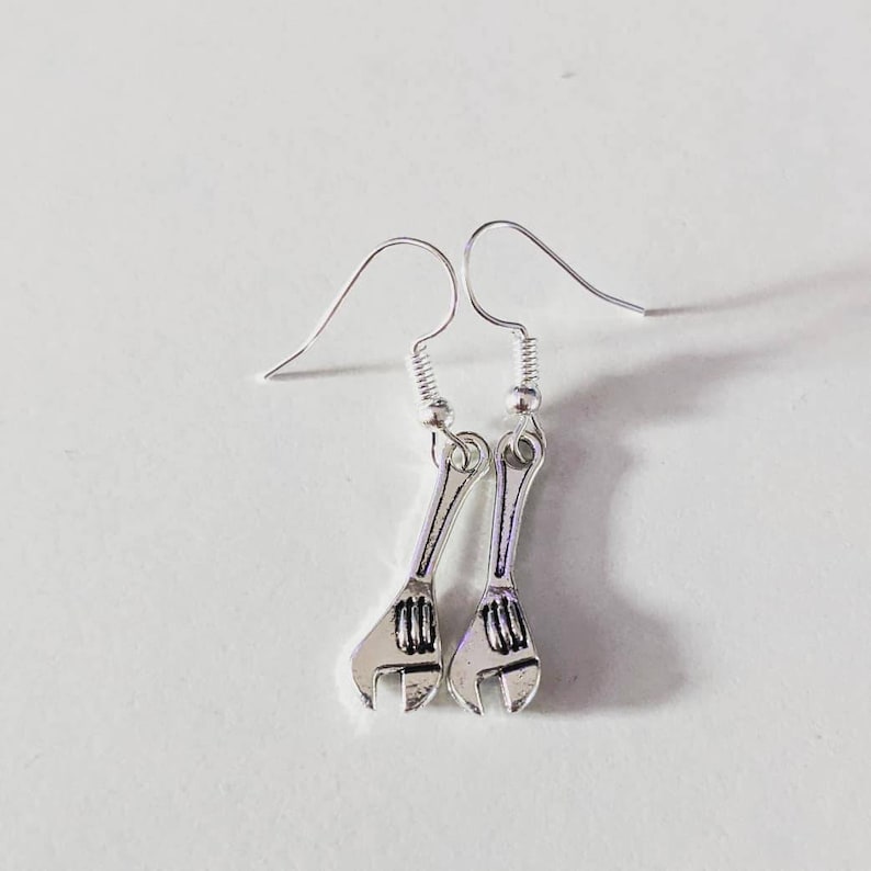 May include: A pair of silver wrench earrings. The earrings are in the shape of a wrench with a silver hook.