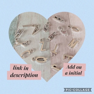 May include: Silver-colored alphabet charms in various letter styles, including the letters H, V, G, B, Z, T, Q, and M. The charms are displayed on a heart-shaped background with text that reads "link in description" and "Add on a initial".