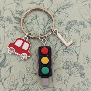 May include: A silver key chain with a red car charm, a traffic light charm with red, yellow, and green lights, and a silver charm with the letter L.