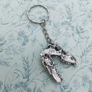 以下が含まれることがあります： シルバーの恐竜の頭蓋骨キーホルダーとシルバーのキーリング。頭蓋骨は詳細に作られており、質感のある表面をしています。