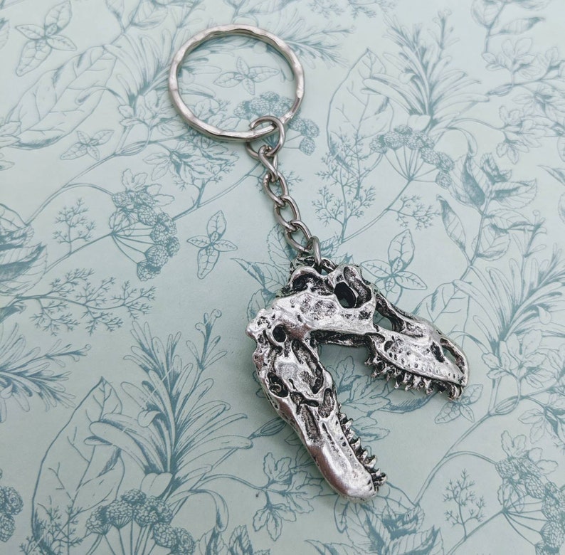 以下が含まれることがあります： シルバーの恐竜の頭蓋骨キーホルダーとシルバーのキーリング。頭蓋骨は詳細に作られており、質感のある表面をしています。