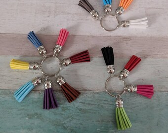May include: A set of colorful tassel keychains with silver rings. The keychains are arranged in a circle with the tassels pointing outwards. The tassels are in various colors, including blue, red, yellow, green, and purple.