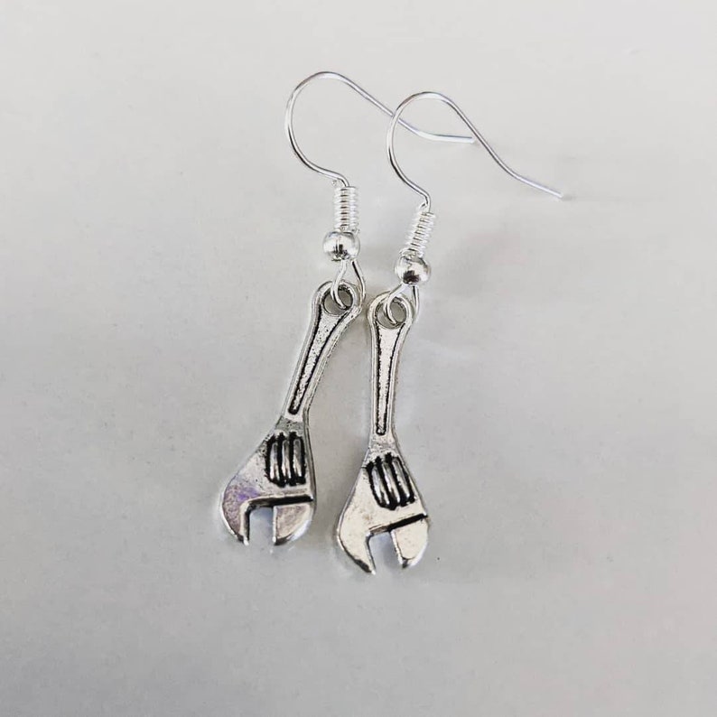 May include: A pair of silver wrench earrings. The earrings are in the shape of a wrench with a silver hook.