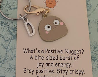May include: A keychain with a charm shaped like a smiling nugget, a silver letter "D" charm, and a card that reads "Positive Nuggets". The card has a cartoon nugget illustration and inspirational text.