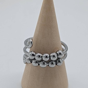 May include: A silver ring with a spiral design and multiple rows of beads.