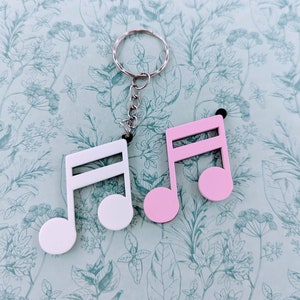 Könnte beinhalten: Ein Schlüsselanhänger in Form von weißen und rosa Noten mit einem silbernen Schlüsselring. Die Noten sind mit einer silbernen Kette am Ring befestigt.