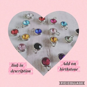 May include: A collection of colorful gemstone charms with silver-colored loops. The charms feature various colors, including red, blue, yellow, pink, and black. The text "link in description" and "Add on birthstone" are also visible.