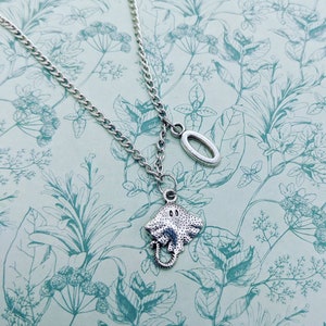 May include: A silver necklace with a silver stingray charm and a silver oval charm. The necklace is on a white background with a floral pattern.