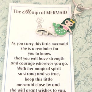 Peut inclure: Un porte-clés avec un charm en forme de sirène et une carte. Le charm de sirène vert et rose est attaché à un porte-clés argenté. La carte indique "The Magical Mermaid" et comprend un poème.