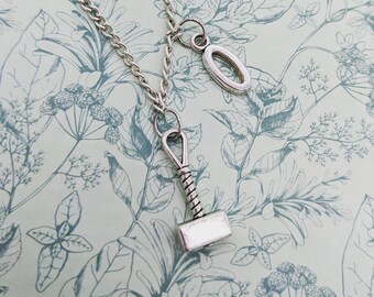 May include: A silver necklace with a hammer charm and a small oval charm. The necklace is on a floral patterned background.