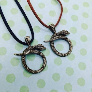 May include: Two bronze snake necklaces with a coiled snake design. One necklace has a black cord and the other has a brown cord.