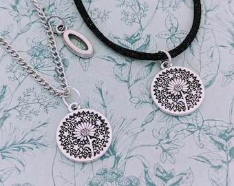 Puede incluir: Dos collares de plata con dijes de diente de león. Un collar es una cadena de plata con un dije ovalado de plata. El otro collar es un cordón negro con un dije de diente de león de plata.
