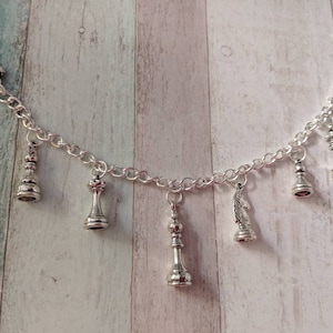 May include: A silver charm bracelet with a variety of chess piece charms, including a king, queen, knight, and pawn. The bracelet has a toggle clasp.