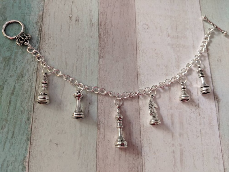 May include: A silver charm bracelet with a variety of chess piece charms, including a king, queen, knight, and pawn. The bracelet has a toggle clasp.