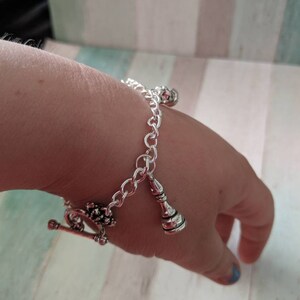 May include: A silver chain bracelet with a silver charm in the shape of a bottle and a silver charm with a floral design.