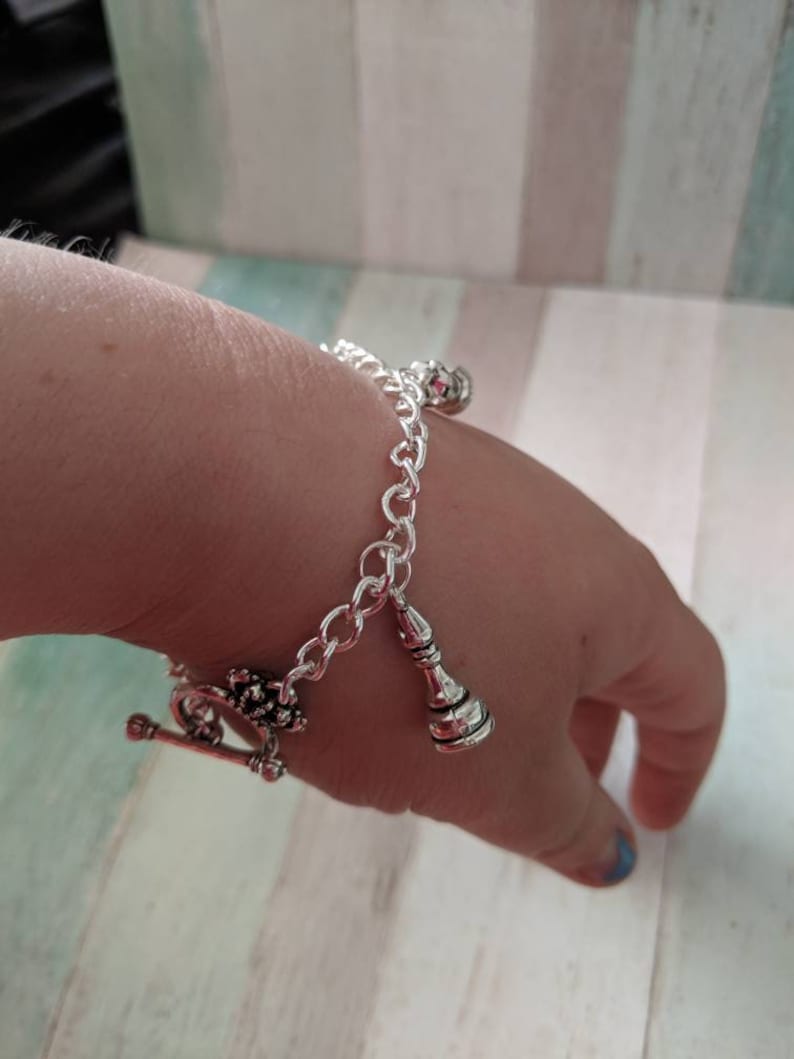May include: A silver chain bracelet with a silver charm in the shape of a bottle and a silver charm with a floral design.