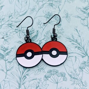 May include: A pair of black metal earrings with red, white and black Pokeball designs.