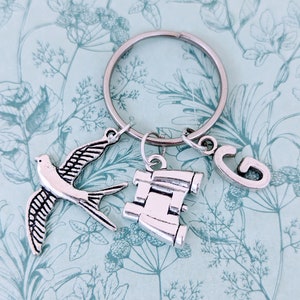 May include: Silver charm keyring with a bird, binoculars, and the letter G. The charms are attached to a silver key ring.