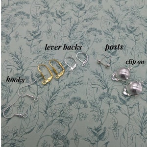 May include: A close-up of earring findings, including lever backs, posts, hooks, and clip-on earrings. The findings are arranged on a floral patterned surface.