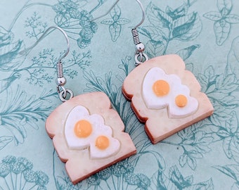 May include: A pair of silver earrings shaped like toast with a fried egg on top. The earrings are made of polymer clay and have a realistic look.