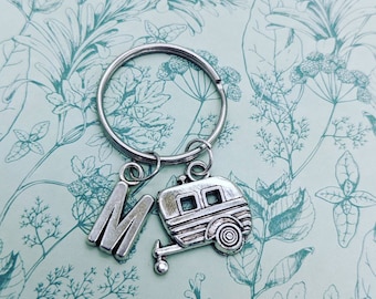 May include: Silver keychain with a letter M charm and a camper charm. The charms are attached to a silver key ring.