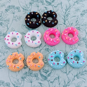 Puede incluir: Surtido de diez mini amuletos con forma de donut con coloridos espolvoreos. Los donuts son de varios colores, incluyendo rosa, azul, blanco, marrón y naranja.