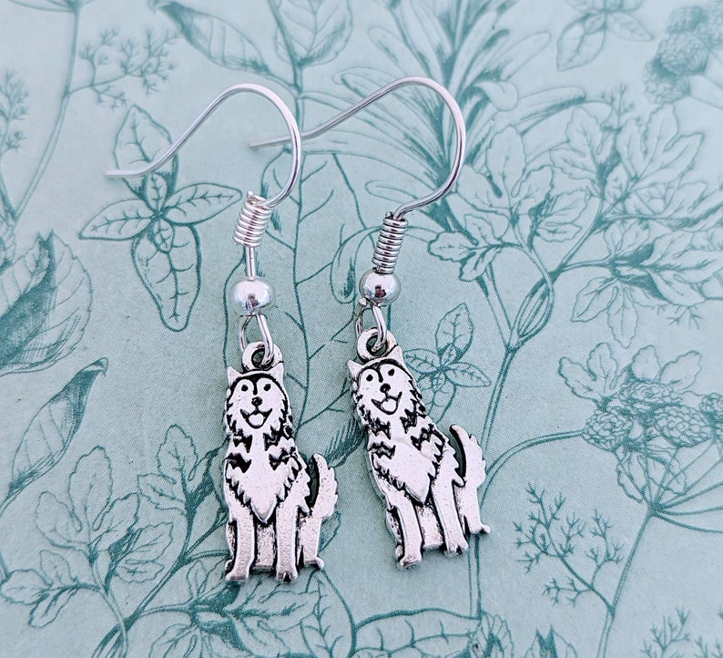 May include: A pair of silver dangle earrings featuring a wolf or husky design. The earrings have a silver hook and a silver spring.