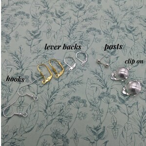 May include: A close-up of earring findings, including lever backs, posts, hooks, and clip-on earrings. The findings are arranged on a floral patterned surface.