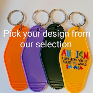 Pode incluir: Quatro chaveiros de cores diferentes com um design de chave de motel. Os chaveiros são laranja, roxo, verde e amarelo. O chaveiro amarelo tem o texto "AUTISMO UMA FORMA DIFERENTE DE VER O MUNDO" e um design de peça de quebra-cabeça arco-íris.