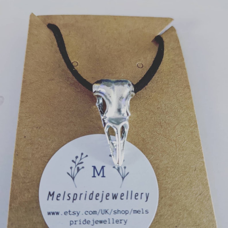 Pu&ograve; includere: Collana con ciondolo a forma di teschio di uccello in argento su un cordoncino nero, esposta su una carta marrone con il testo "Mels pridejewellery www.etsy.com/UK/shop/mels pridejewellery"