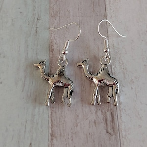 May include: A pair of silver dangle earrings featuring a camel design. The earrings have a hook fastening.