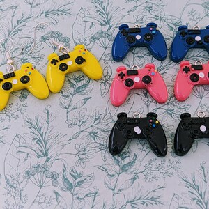 May include: A set of ten colorful video game controller earrings. The earrings are made of plastic and feature a variety of colors, including yellow, blue, pink, and black. Each earring is shaped like a video game controller and has a small loop at the top for attaching to an earring hook.