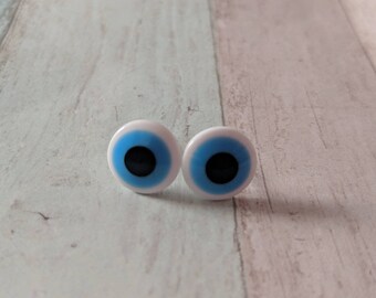 May include: Two large googly eyes with white pupils, blue irises, and black centers. The eyes are on a light wood background.