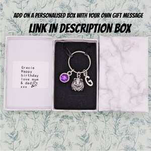 May include: A small gift box with a personalized message for Gracie. The box contains a keychain with a purple crystal charm, a lion charm, and a letter G charm.