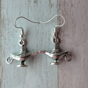 Op de afbeelding: Een paar zilveren oorbellen met een gedetailleerd ontwerp van een genielamp. De lampen hebben een decoratief swirl-patroon en een kleine lus aan de zijkant.