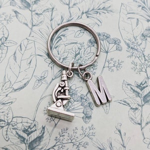 May include: Silver keychain with a microscope charm and a letter M charm. The charms are attached to a silver key ring.
