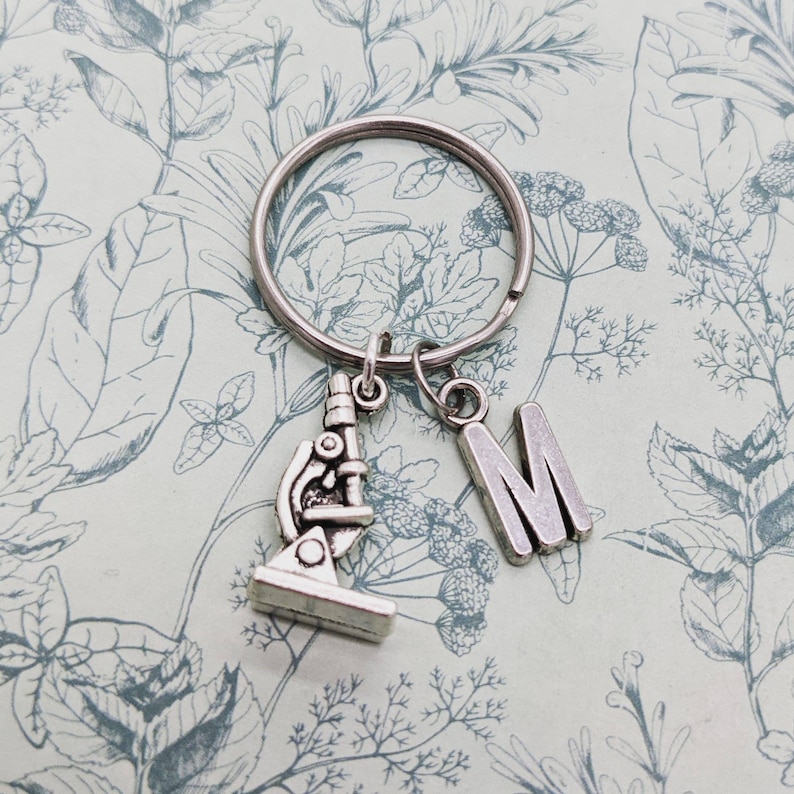 May include: Silver keyring with a microscope charm and a letter M charm. The charms are attached to a silver key ring.
