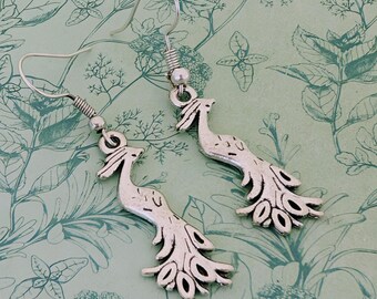 May include: A pair of silver-colored peacock earrings. The earrings feature a detailed peacock design with a long neck and a fanned tail. The earrings are suspended from a simple hook.