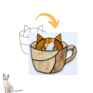 May include: Stained glass cat peeking out of a teacup. The cat has orange and white fur, with clear glass eyes. The teacup is a light brown color with a handle. A line drawing of a cat in a teacup is next to the stained glass.