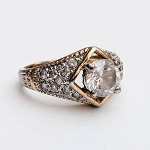 Op de afbeelding: Een gouden ring met een grote, heldere steen omringd door kleinere, heldere stenen.